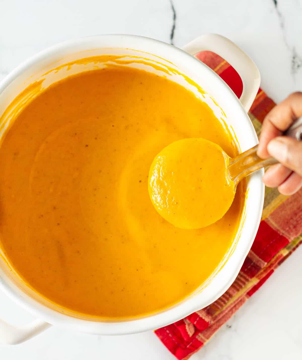 A saucepan with pumpkin soup and a ladleful being taken out.