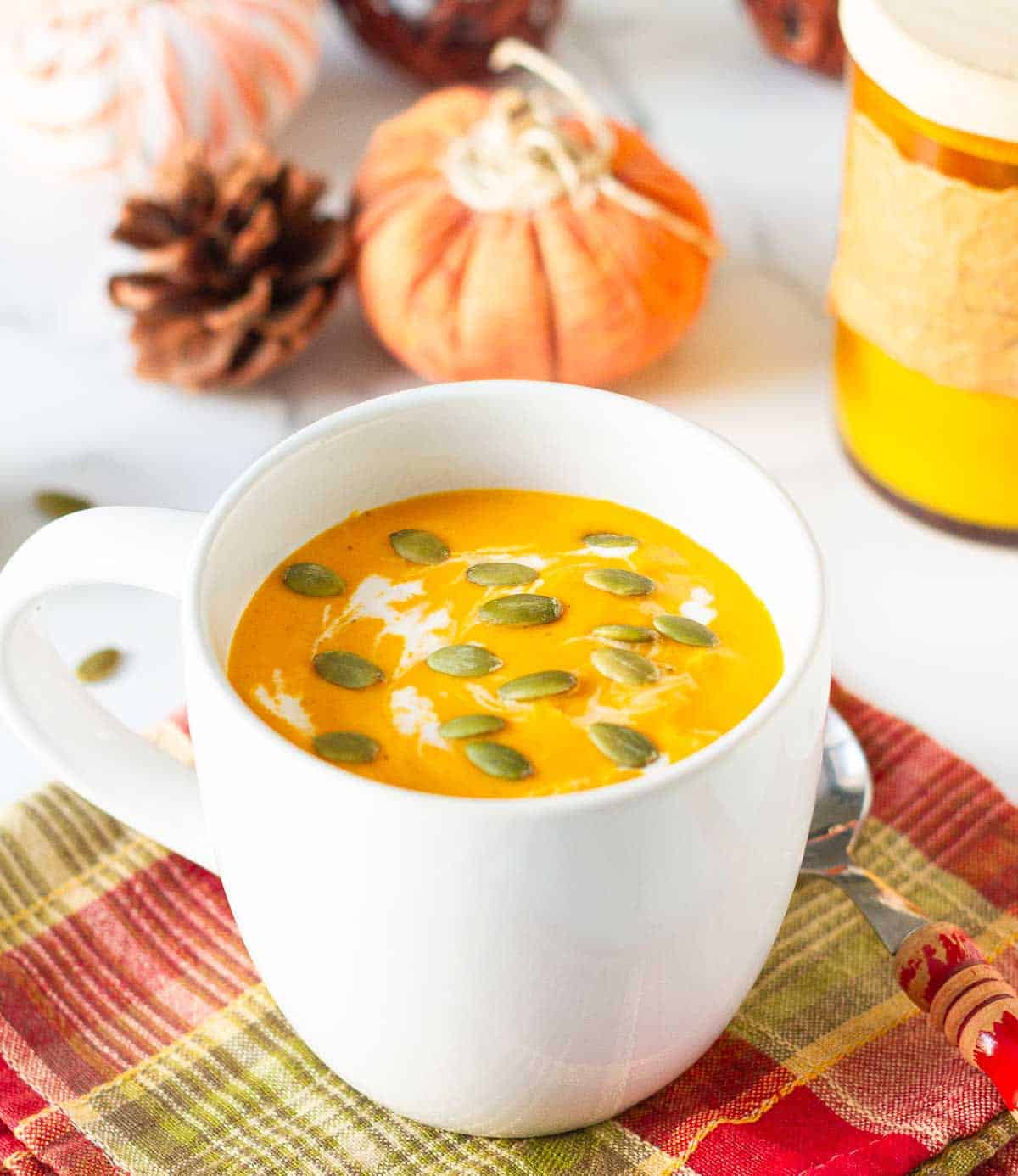 roasted pumpkin soup in a white soup mug on a checkered napkin.