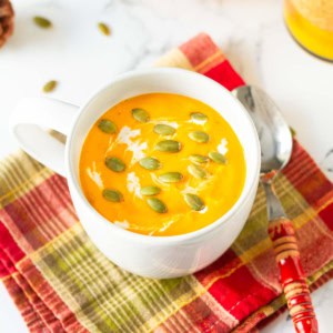 roasted pumpkin soup in a white soup mug with a spoon on a red check napkin.
