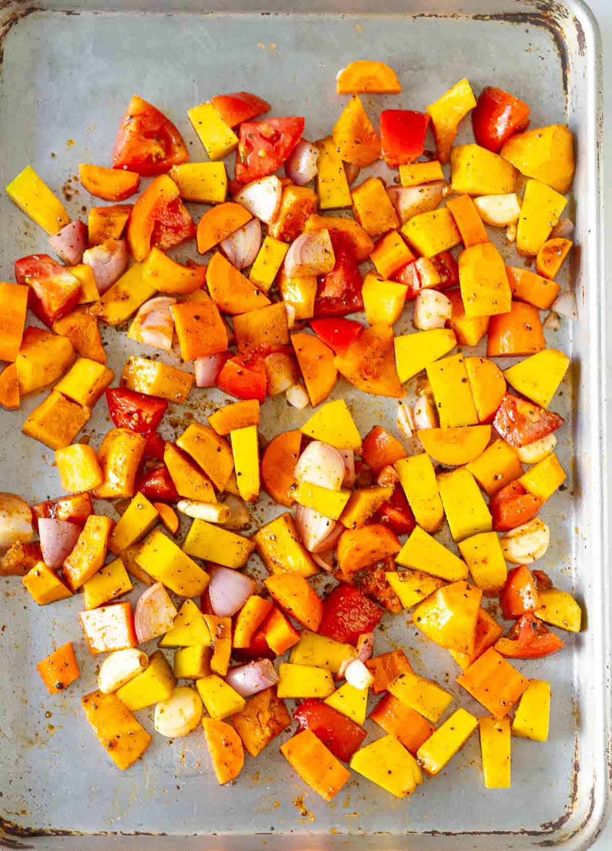 Chopped vegetables tossed with olive oil and seasonings on a baking tray.