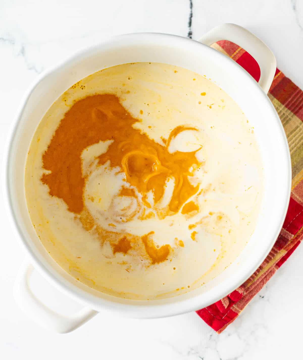 roasted pumpkin soup in a saucepan with coconut milk on top.