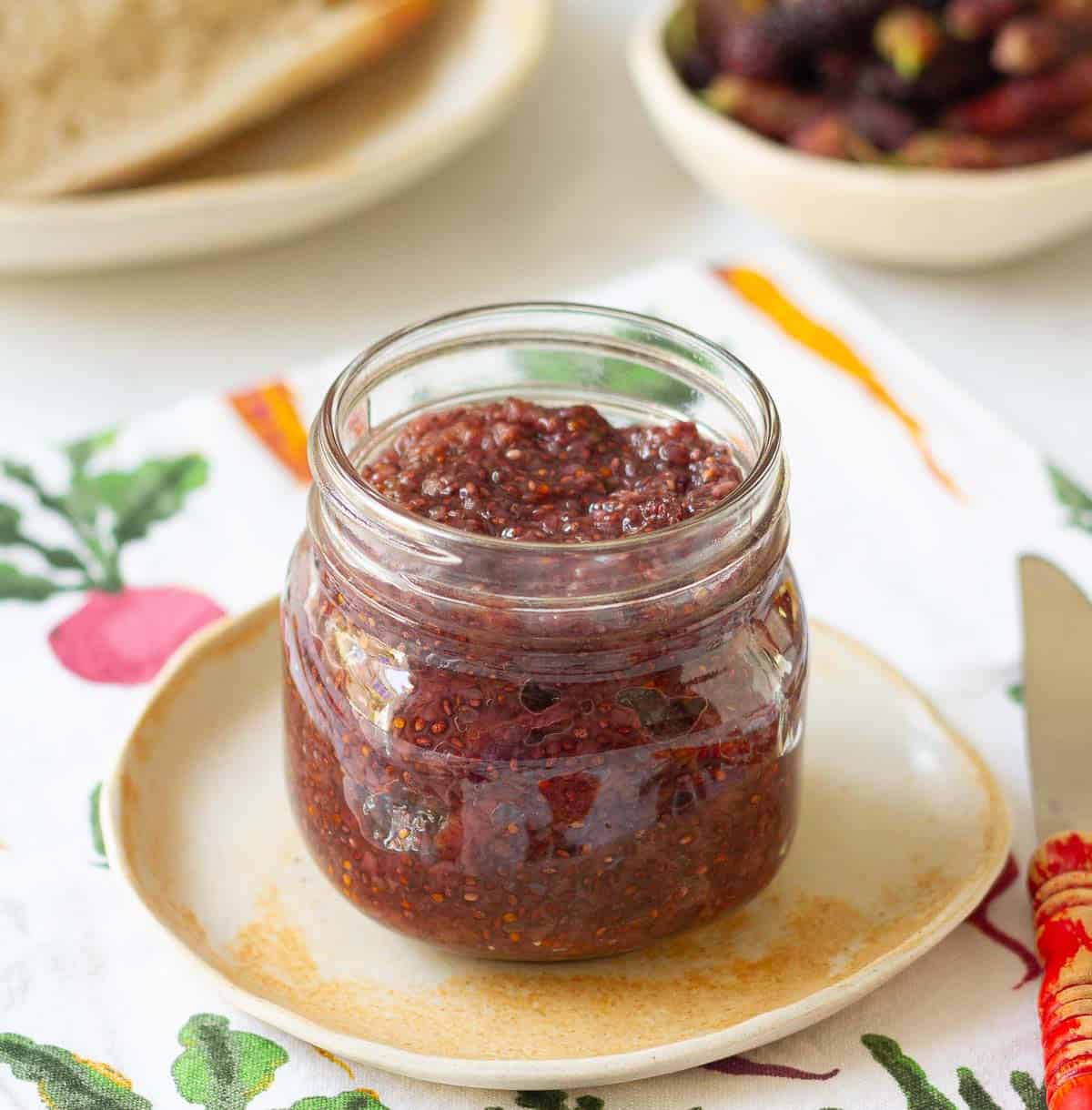 Mulberry jam in a glass jar on a small plate.