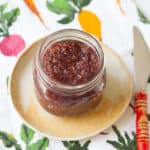 Mulberry jam in a glass jar with a red knife on the side.