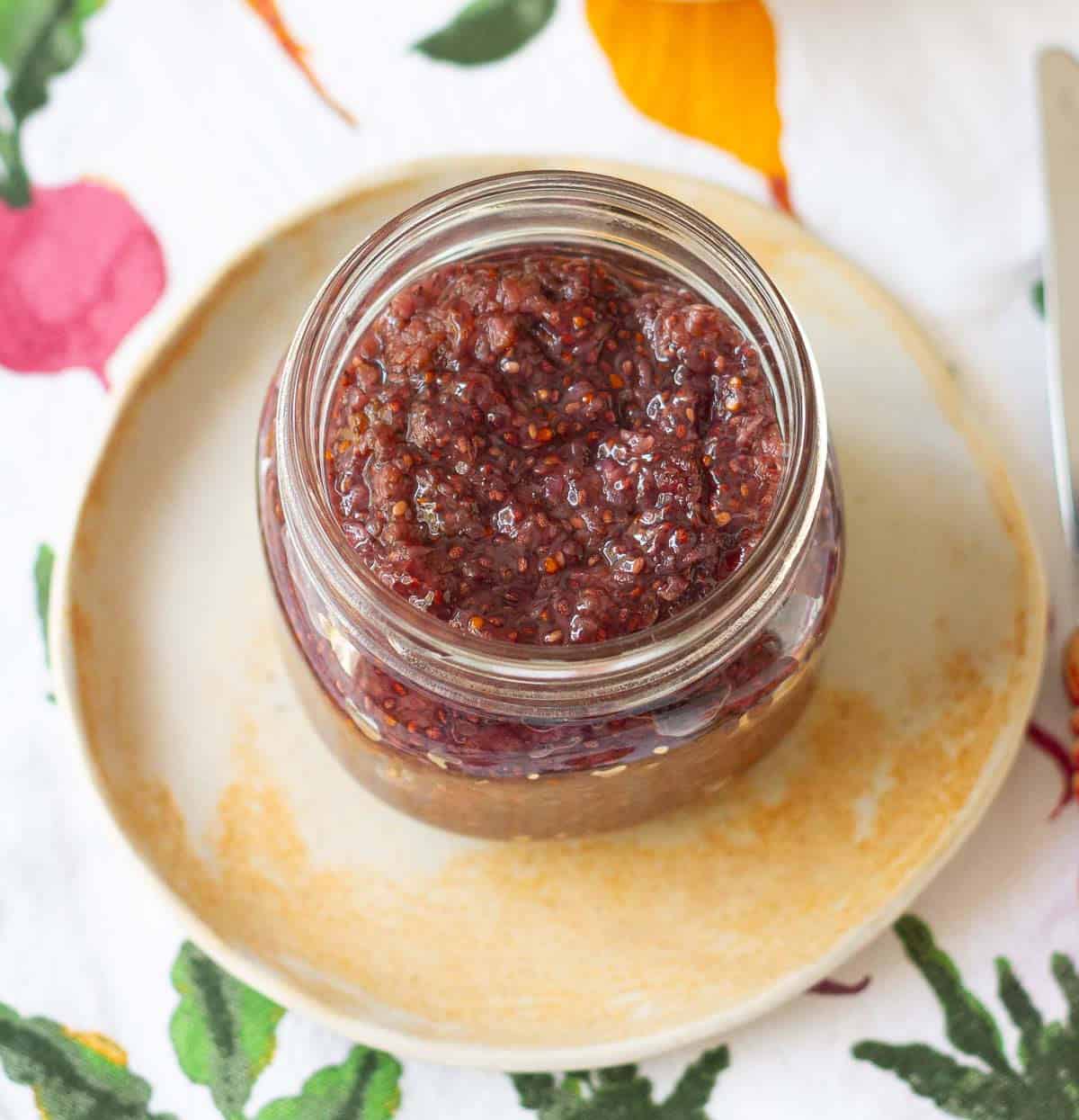 Mulberry jam in a glass jar placed on a small plate.