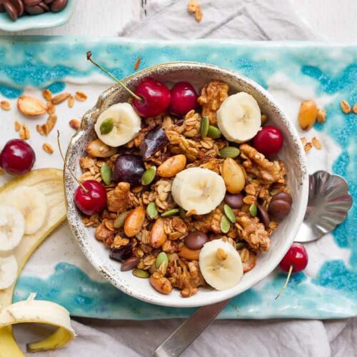 Banana granola in a bowl on a blue tray with sliced bananas on top.