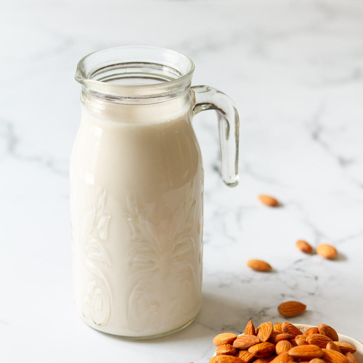 almond milk in a glass pitcher with almonds scattered around.