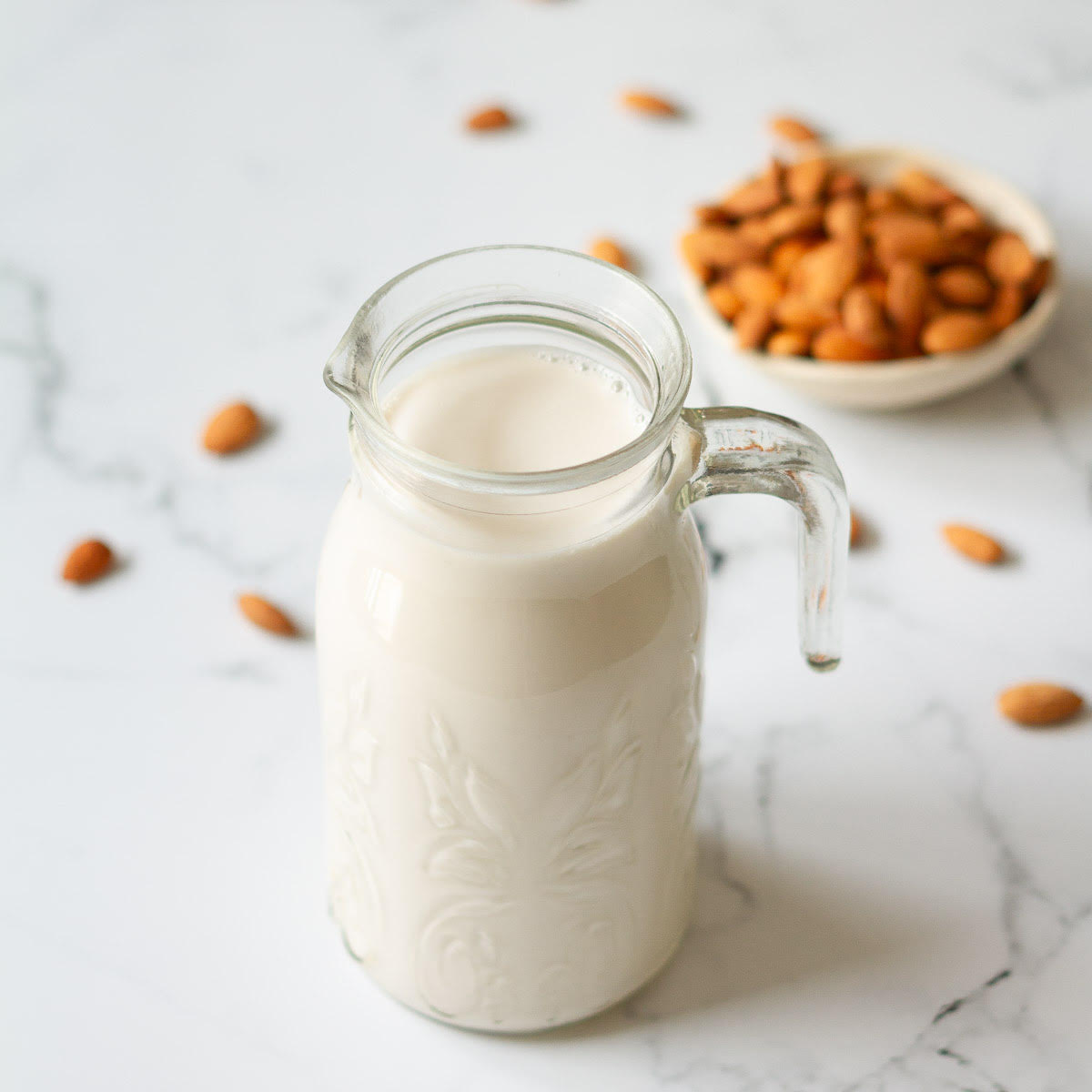 almond milk in a glass pitcher with almonds in the background.