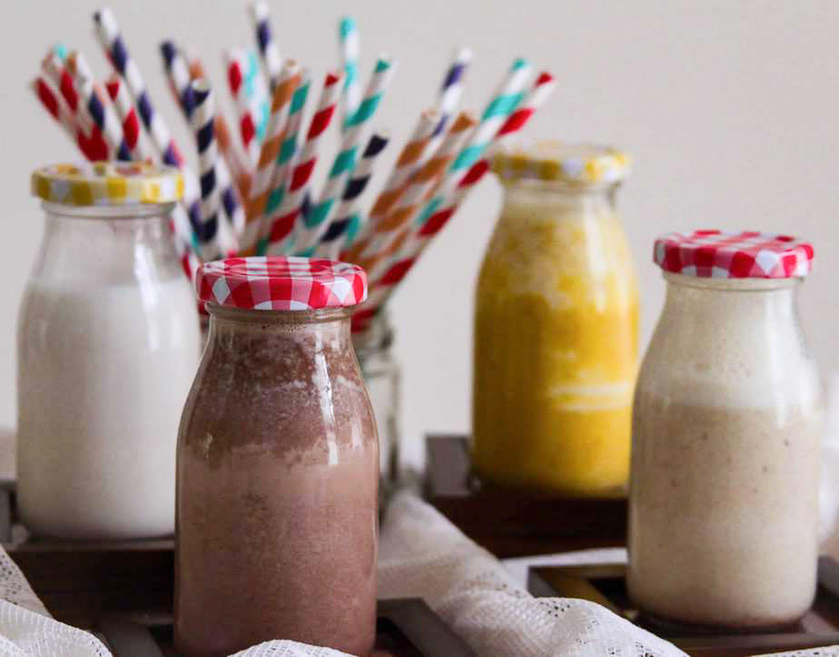 flavored almond milk in glass bottles w/ lids and colorful paper straws in the background.