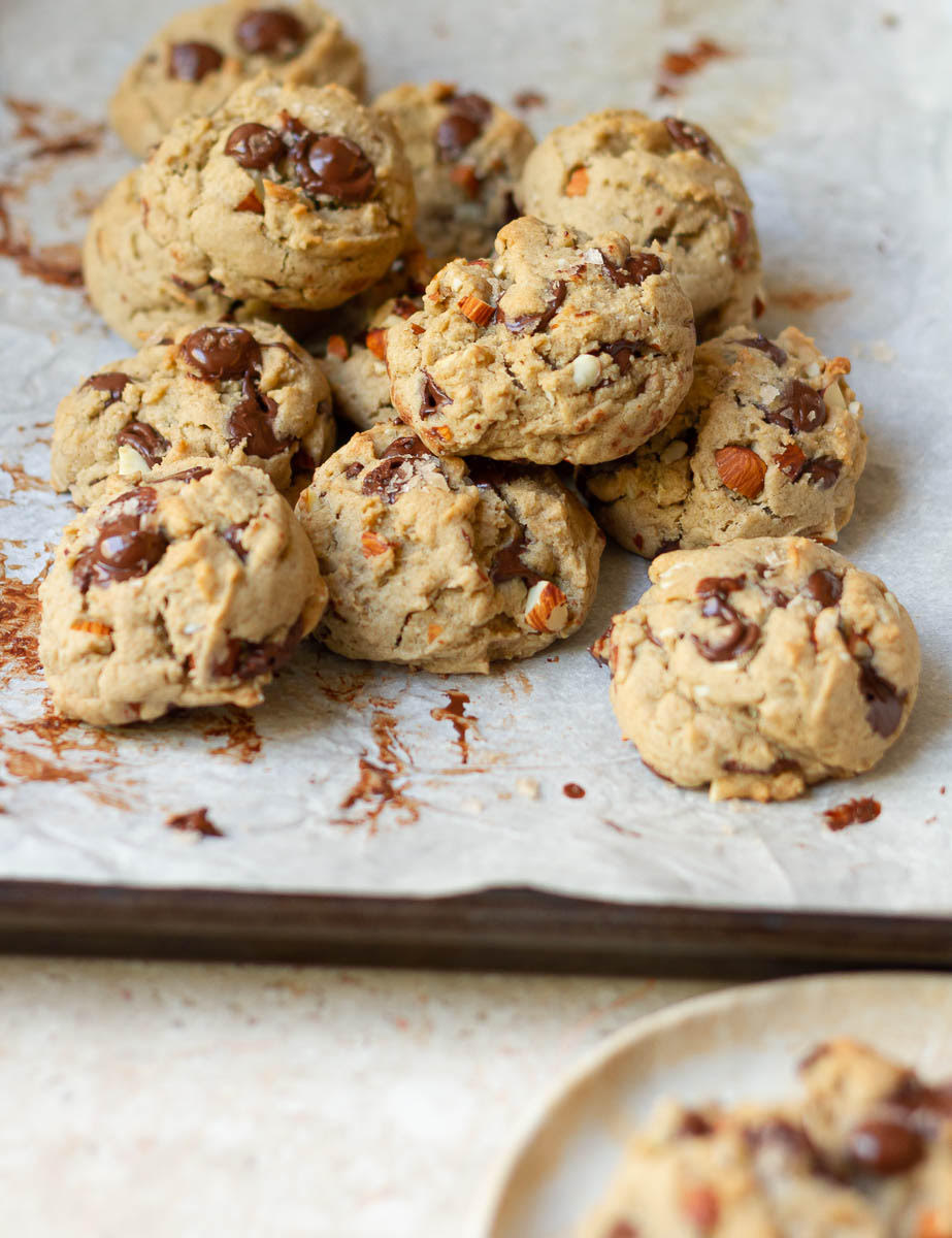 Chocolate chip cookies with almonds stacked on a parchment-lined tray.