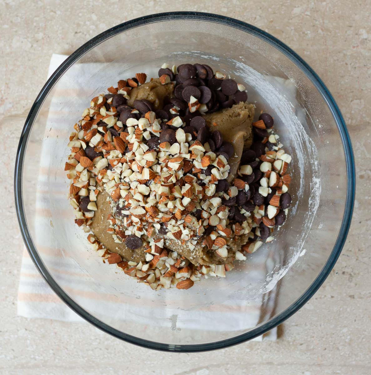 Chocolate chips and chopped almonds on top of cookie dough in a mixing bowl.