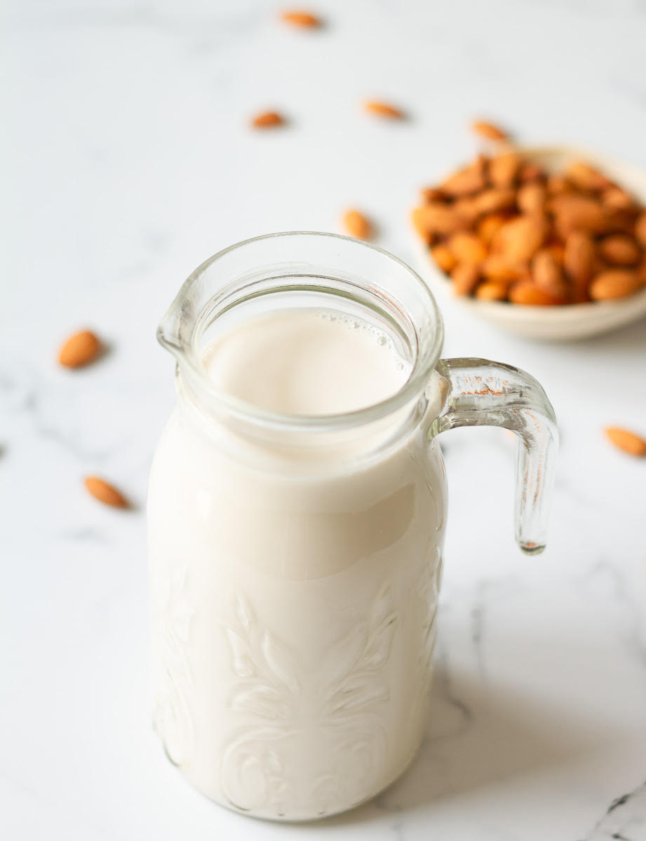 almond milk in a glass pitcher with almonds in the background.