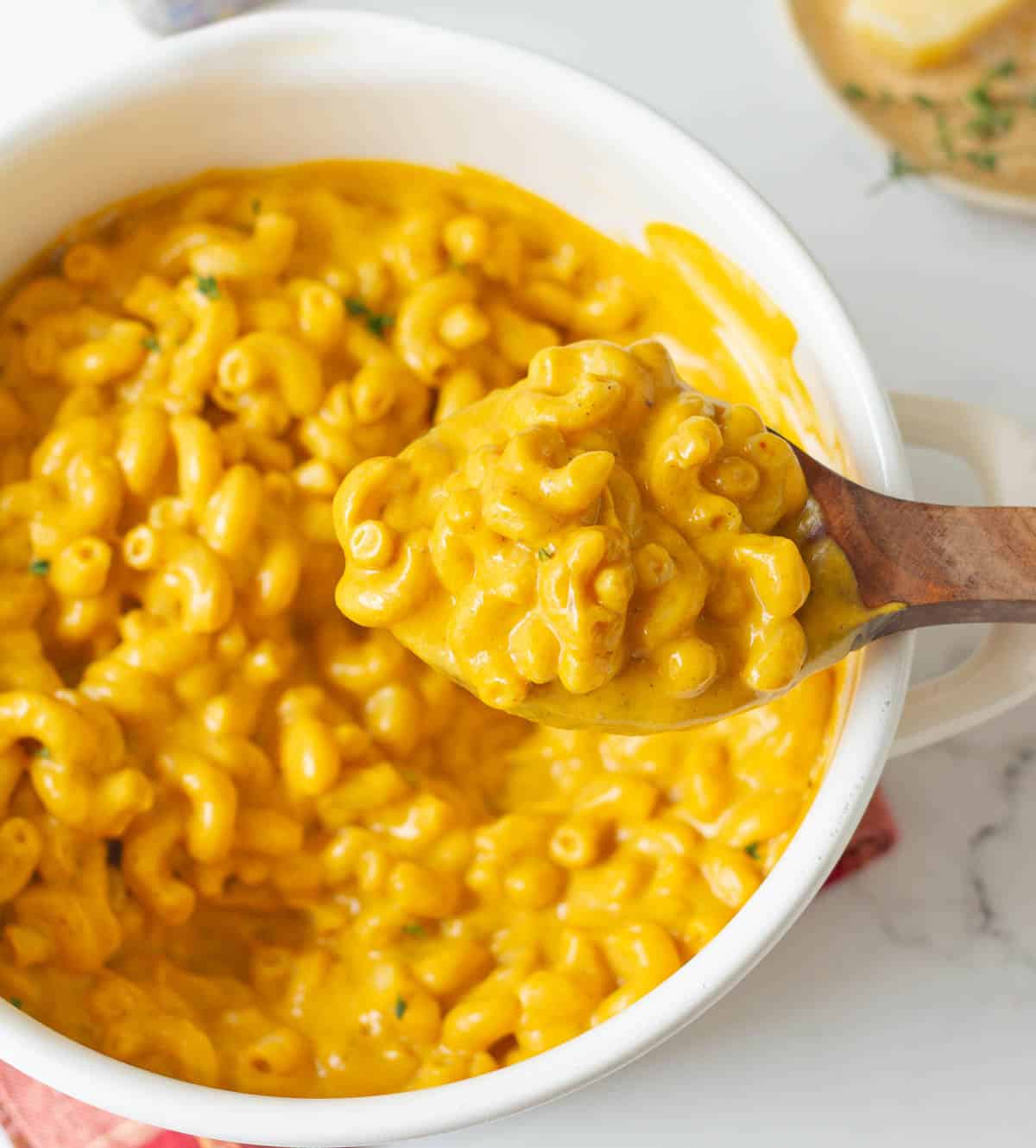 A wooden serving spoon with pasta on top of a pot full of pasta.