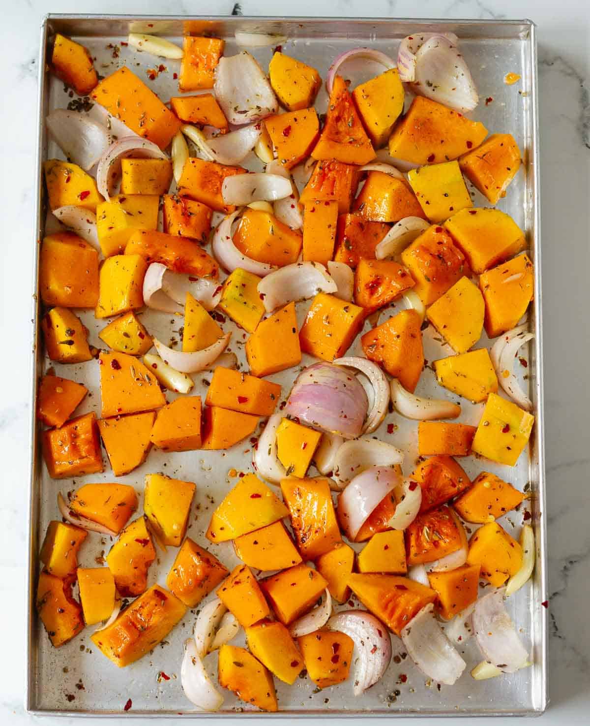 Cubed pumpkin, garlic, and onions on a baking tray.