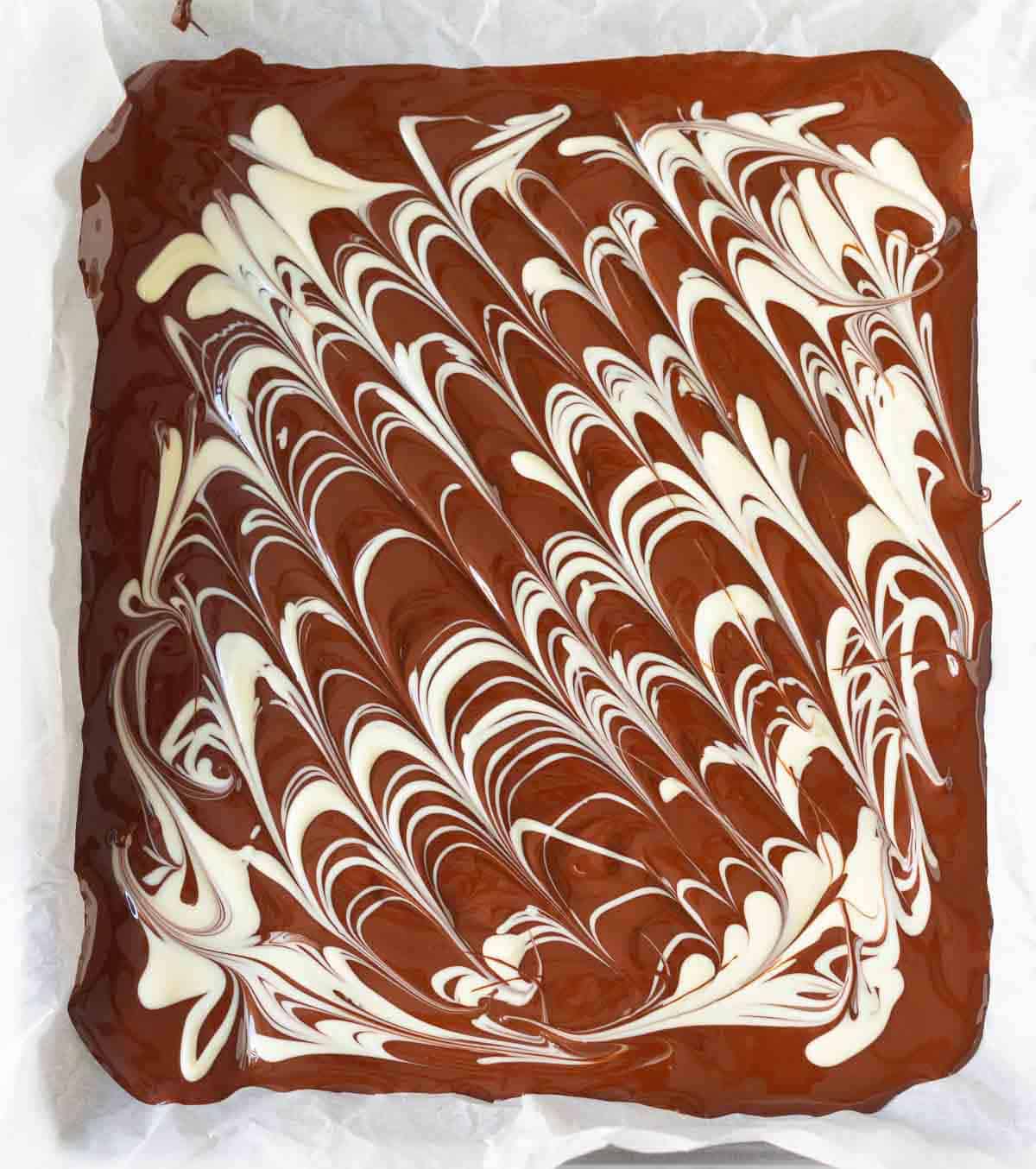 melted dark chocolate on a parchment-lined tray with swirls of melted white chocolate.