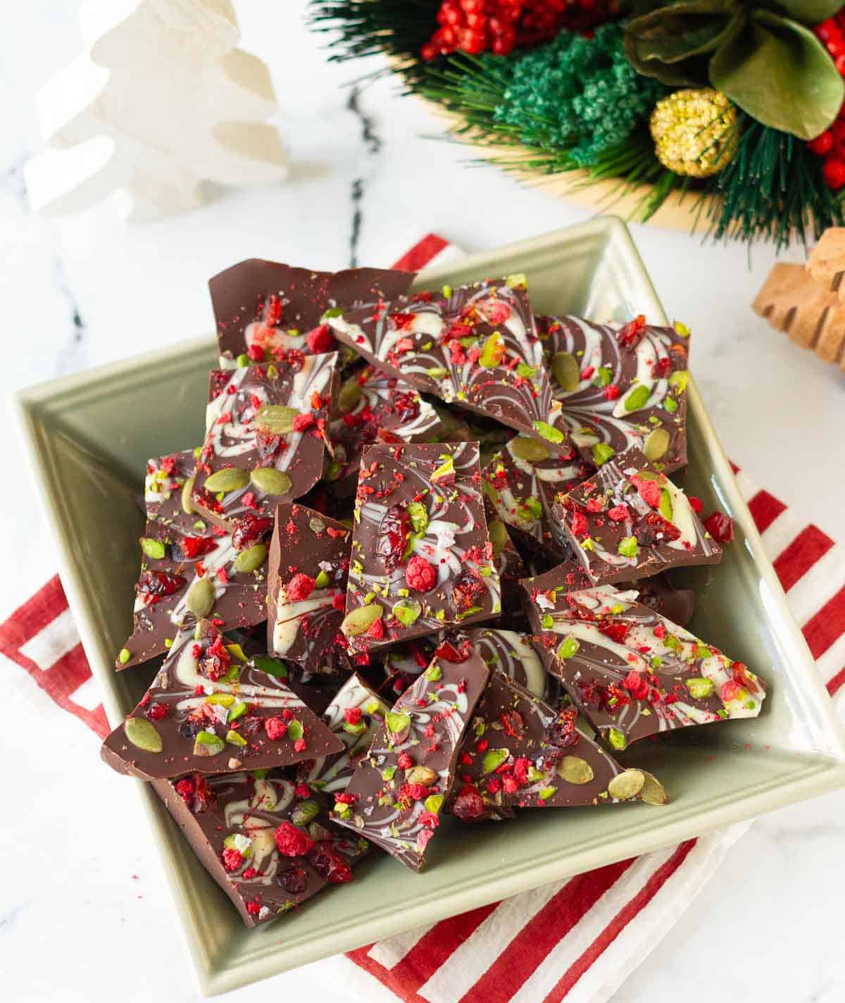 pieces of dark chocolate bark in a green square bowl on a red striped napkin.