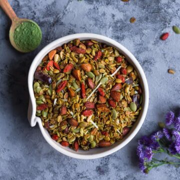 Matcha Granola in a ceramic bowl with a spoonful of matcha and flowers on the side.