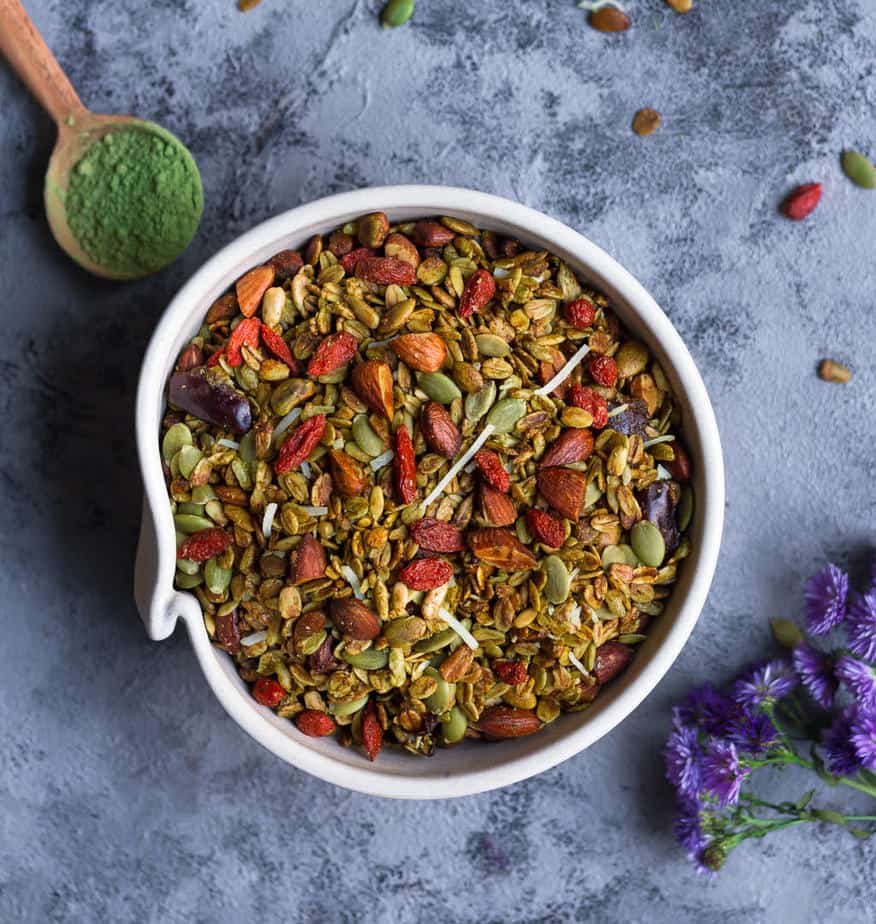 Matcha Granola in a ceramic bowl with a spoonful of matcha and flowers on the side.