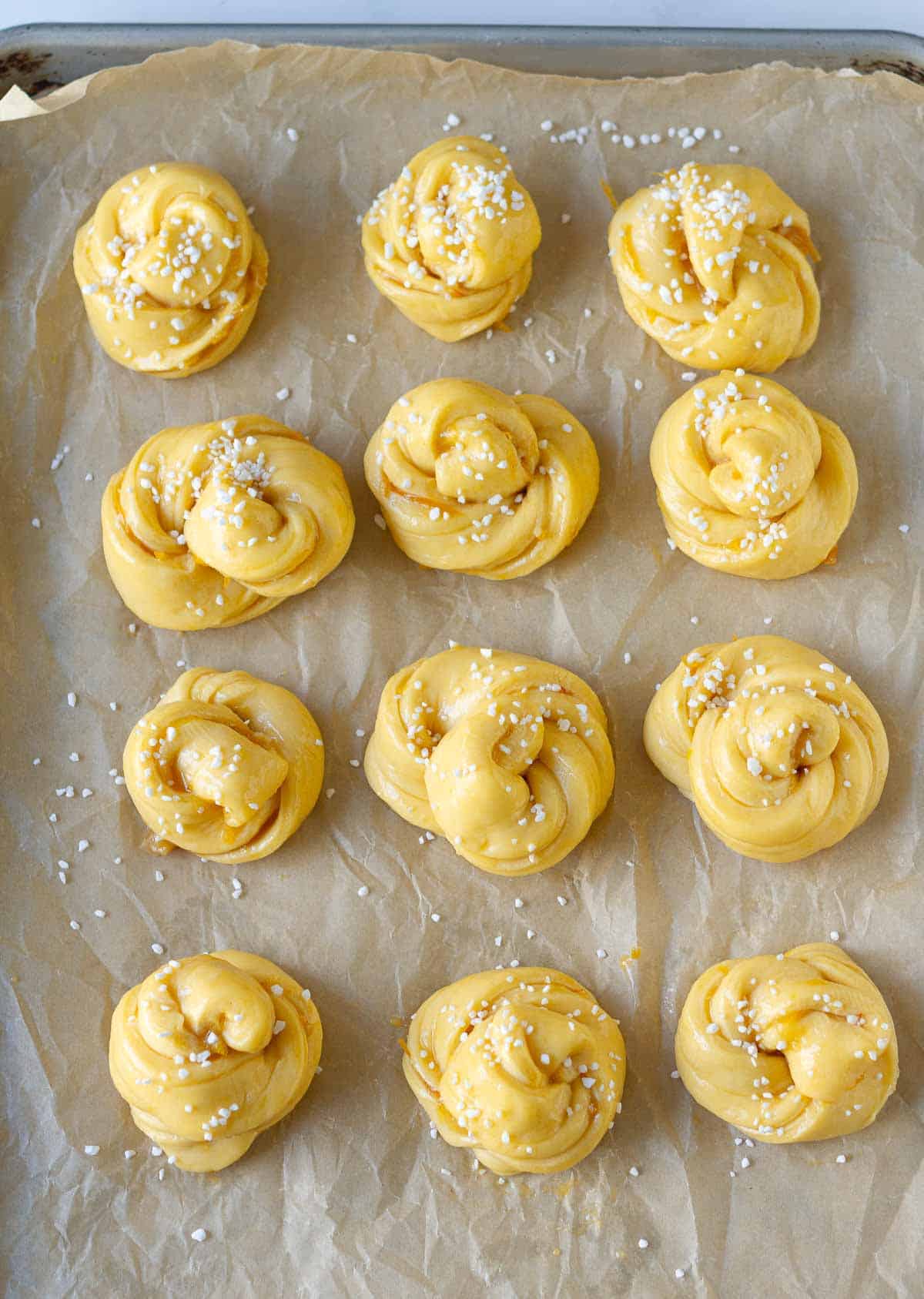 Brioche rolls topped with sugar pearls on parchment paper lined tray.