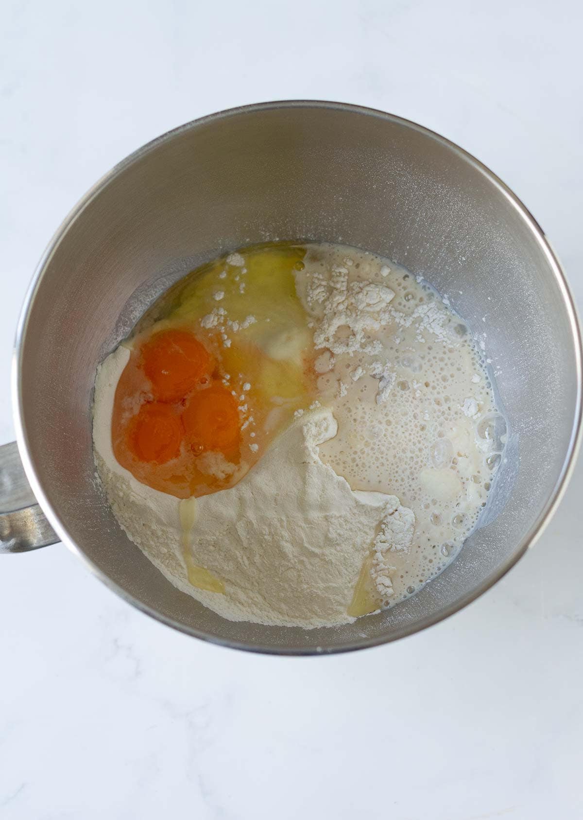 Eggs, flour, yeast mixture in the bowl of a stand mixer.