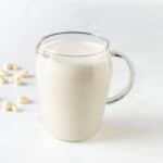 cashew milk in a glass pitcher with some cashews in the background.