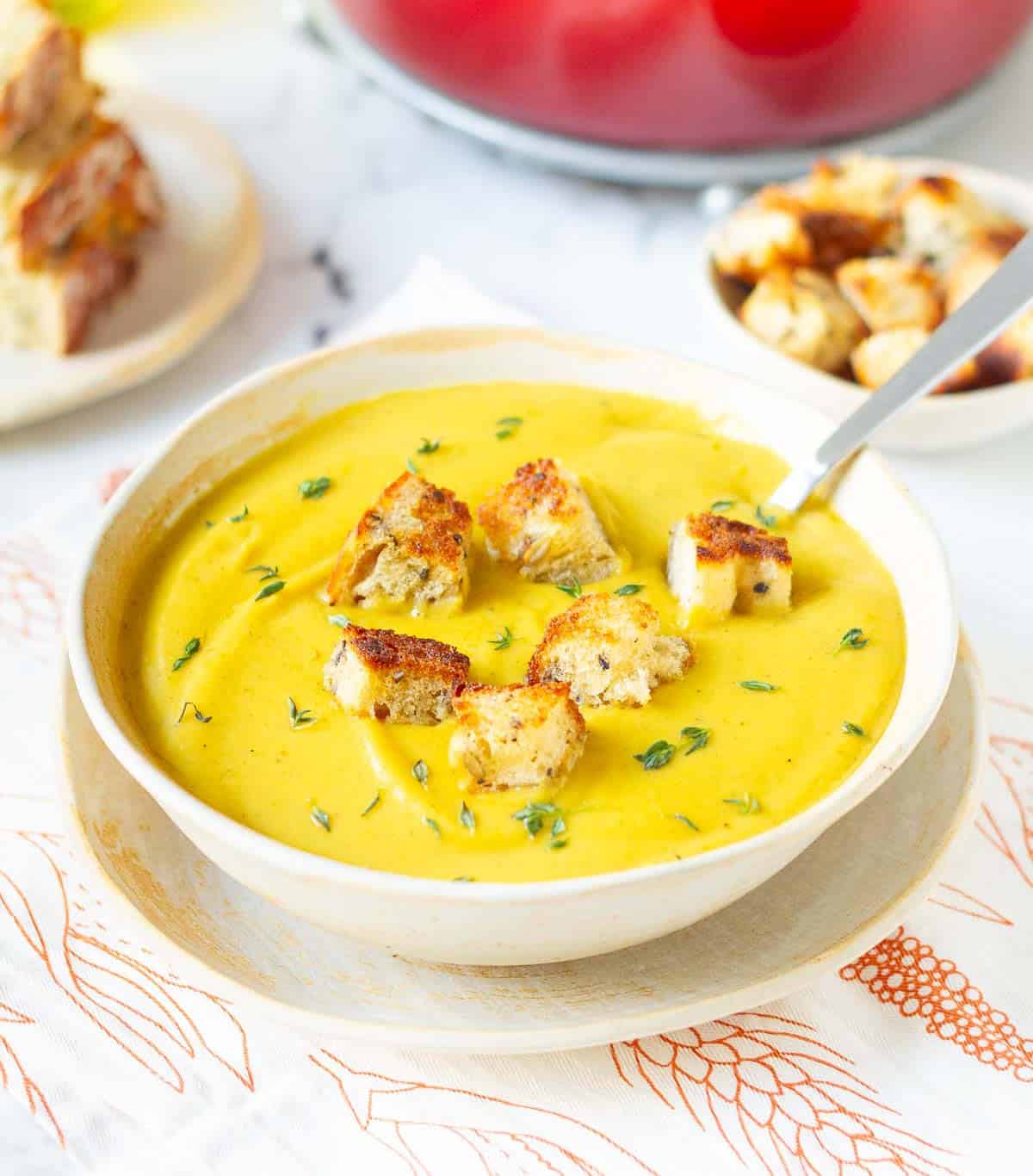 roasted sweet potato soup in a bowl with a spoon, topped with croutons and fresh thyme.