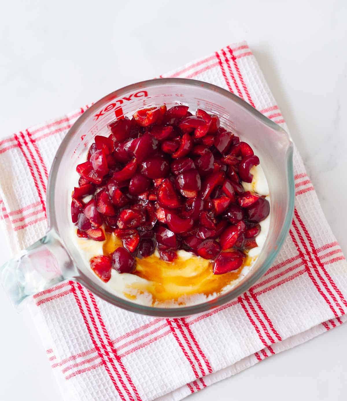 Chopped cherries on yogurt and honey mixture in a measuring cup.