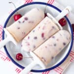 3 cherry popsicles in a bowl with ice and fresh cherries.