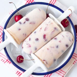 3 cherry popsicles in a bowl with ice and fresh cherries.