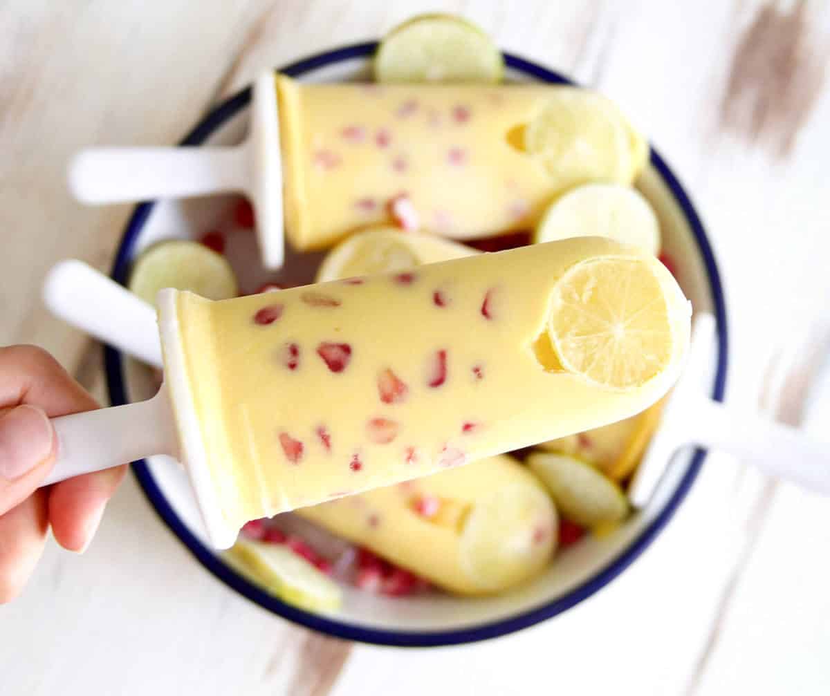 One popsicles with pomegranates and lemon slices held up to show texture.