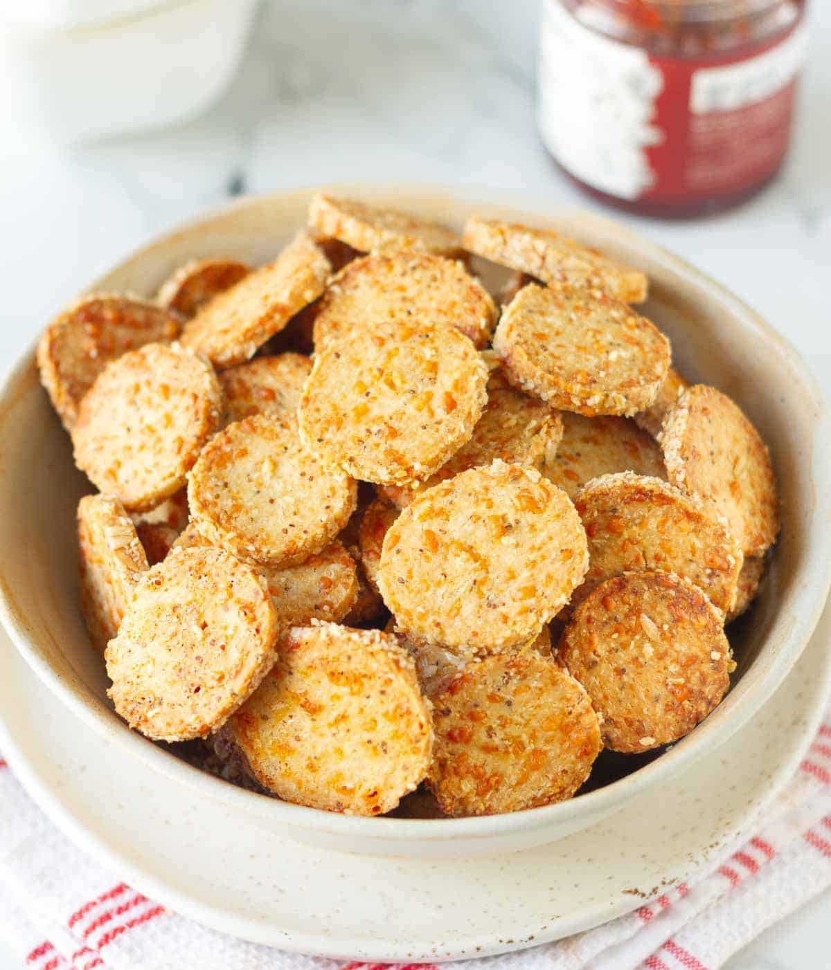 Cheese crackers in a bowl with a jar in the background.