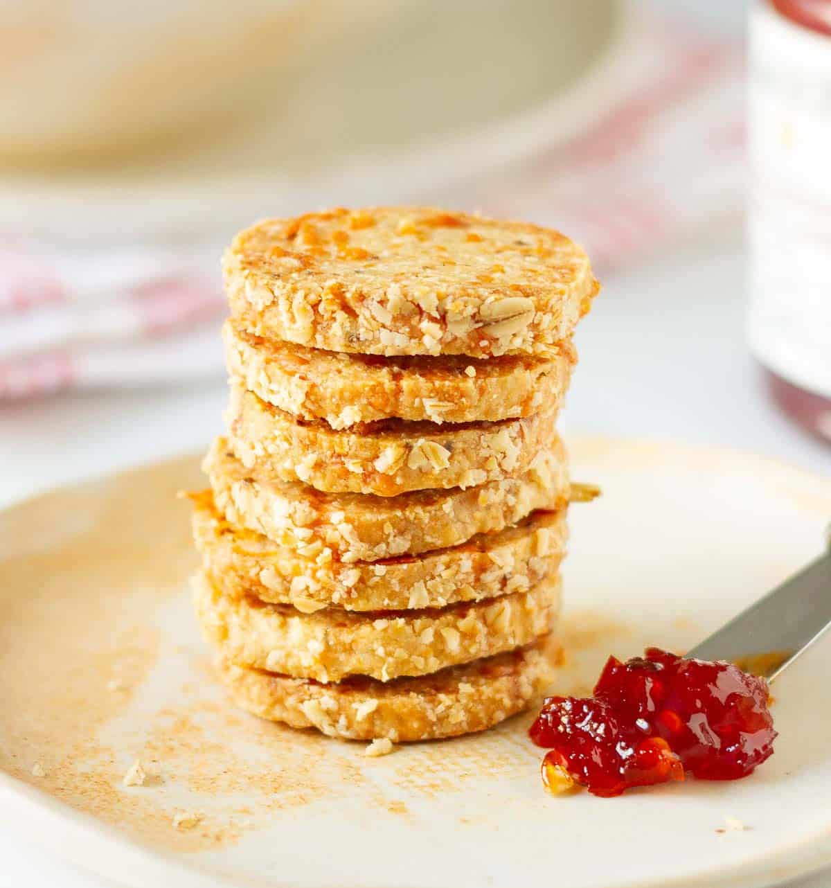 A stack of crackers with a spoon of red pepper jelly on the side.