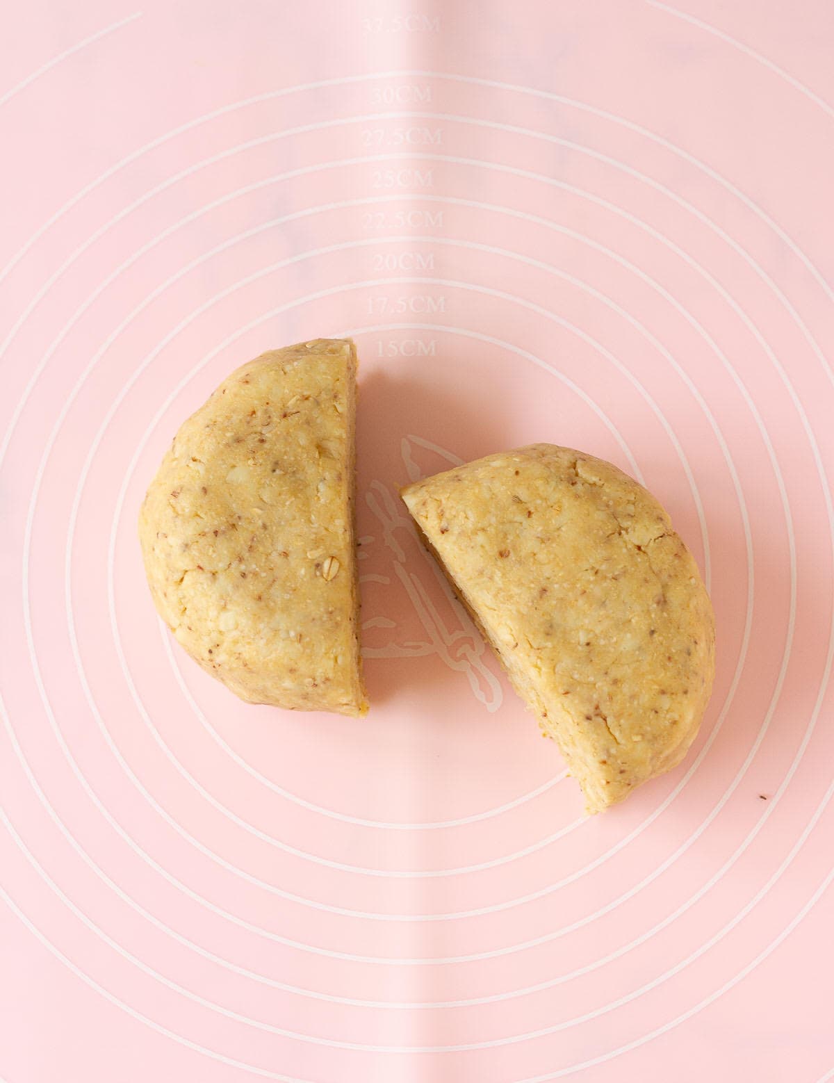 Dough cut into 2 halves on a pink silicone mat.