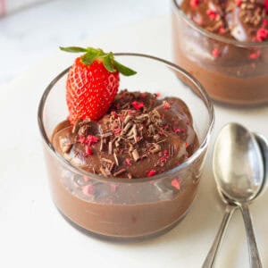 avocado chocolate mousse in a glass cup with 2 spoons on the side.