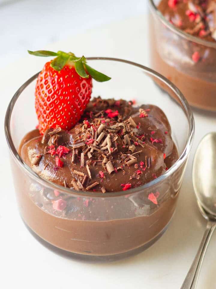 avocado chocolate mousse in a glass cup with 2 spoons on the side.