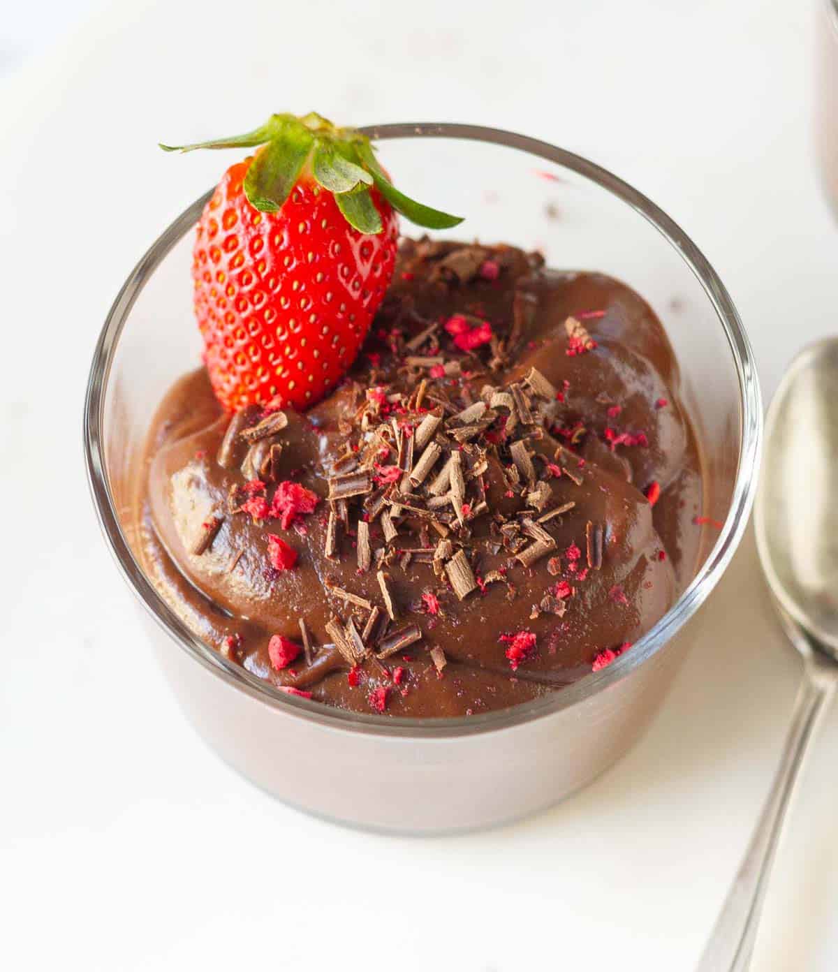 chocolate mousse in a glass cup topped with strawberry, chocolate shavings, and freeze dried raspberries.