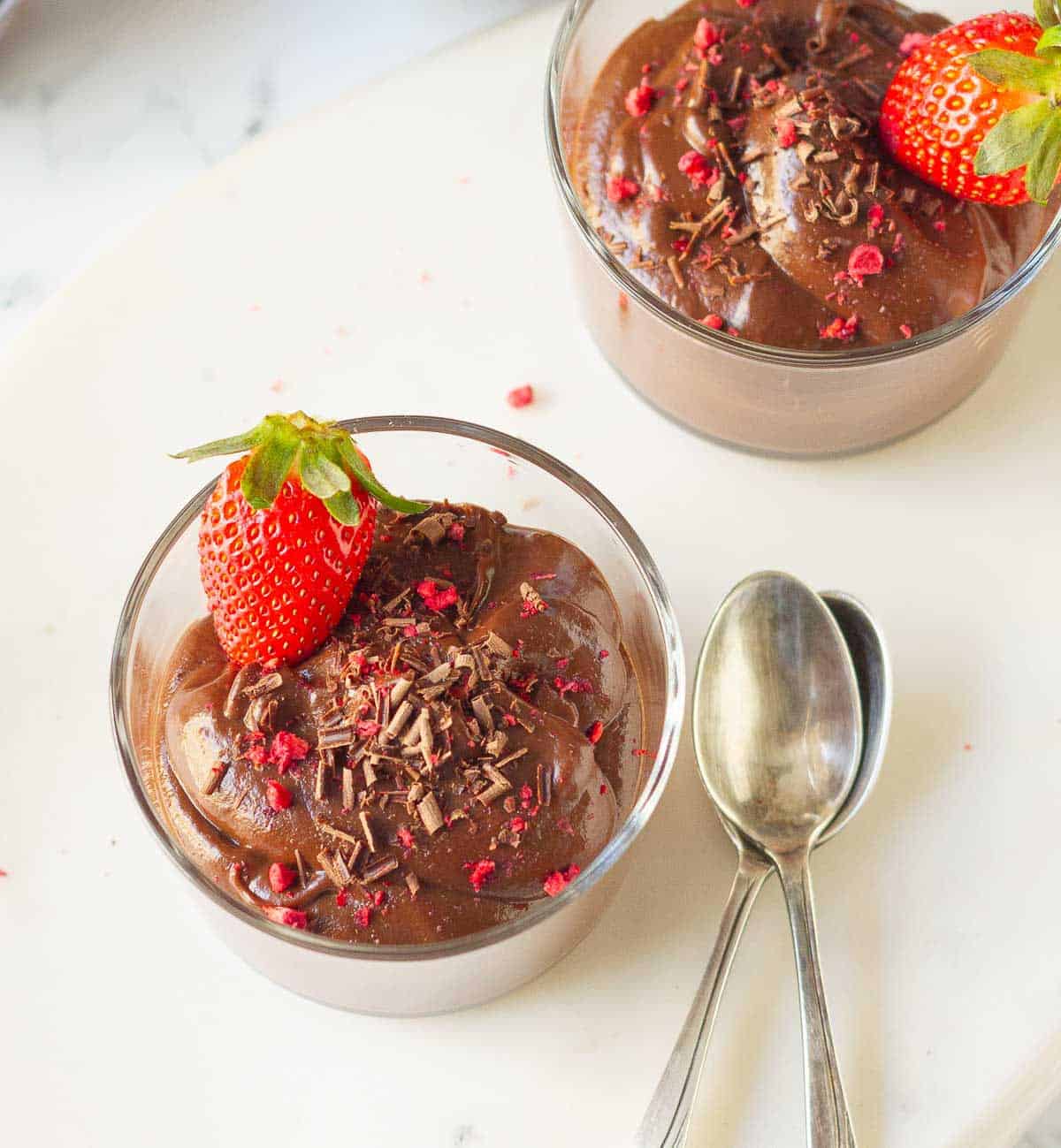 2 bowls of chocolate mousse with 2 spoons on the side.