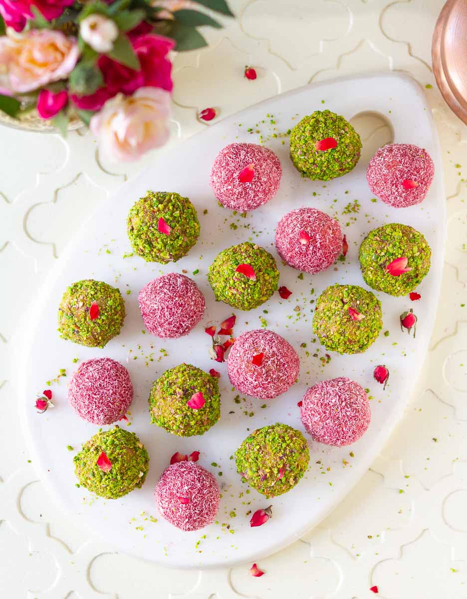 Bliss balls coated with chopped pistachio and pink colored desiccated coconut on a white platter.