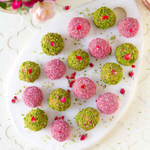 Bliss balls coated with chopped pistachio and pink colored coconut on a white tray.