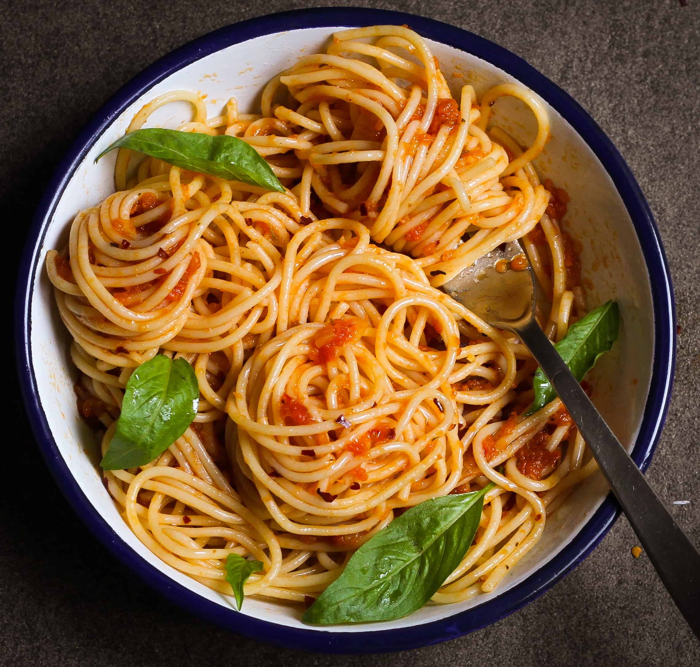 A bowl of spaghetti with tomato sauce and basil on top.