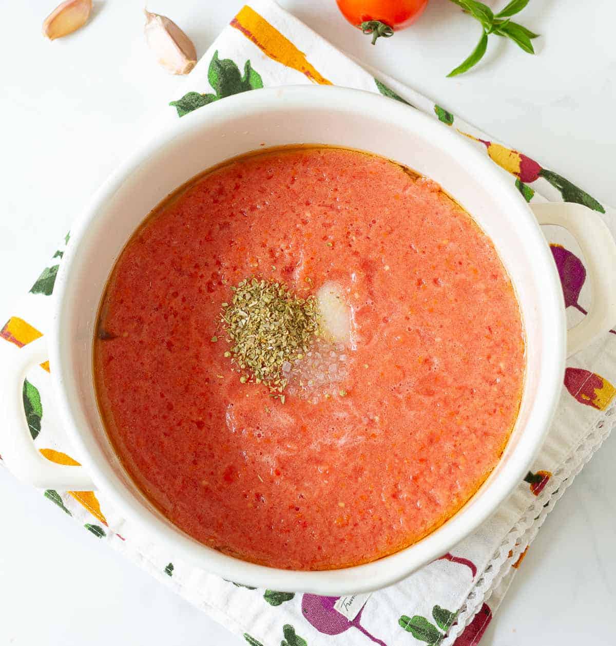 Tomato puree in a pot with salt, dried oregano, and sugar on top.