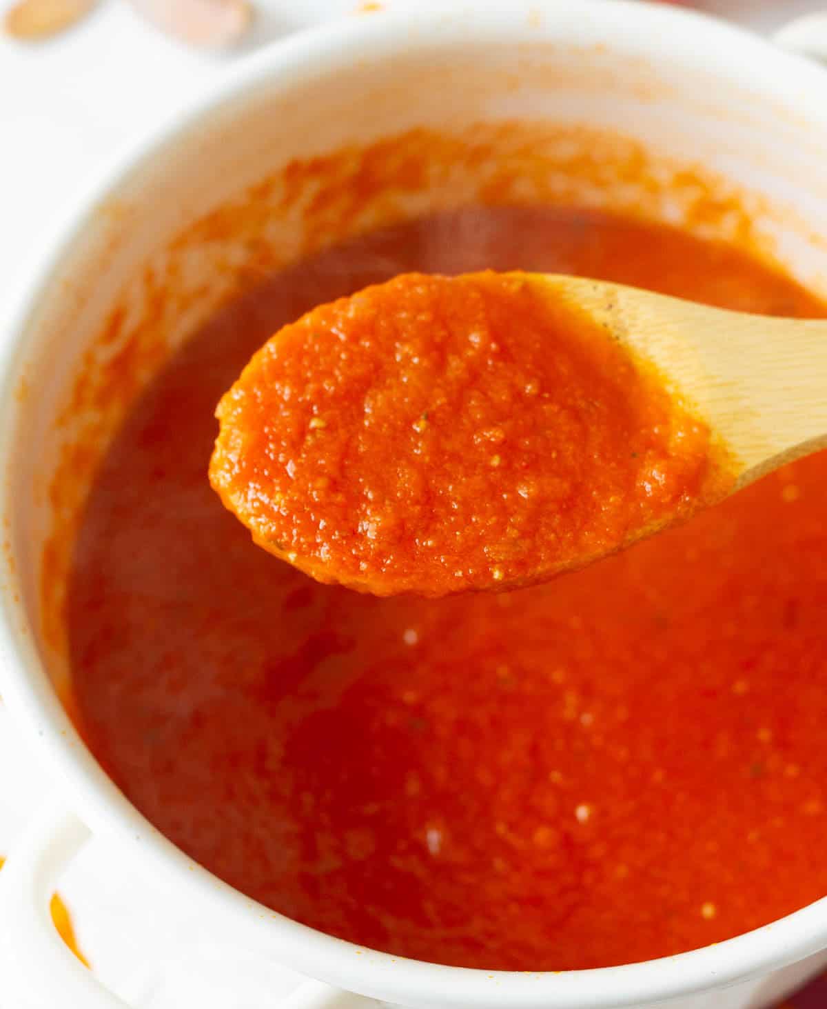 Tomato sauce on a wooden spoon scooped out of a pot.