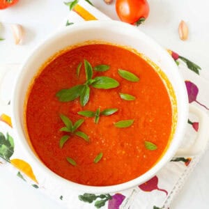 A white stockpot with tomato sauce topped with basil leaves with ingredients around.