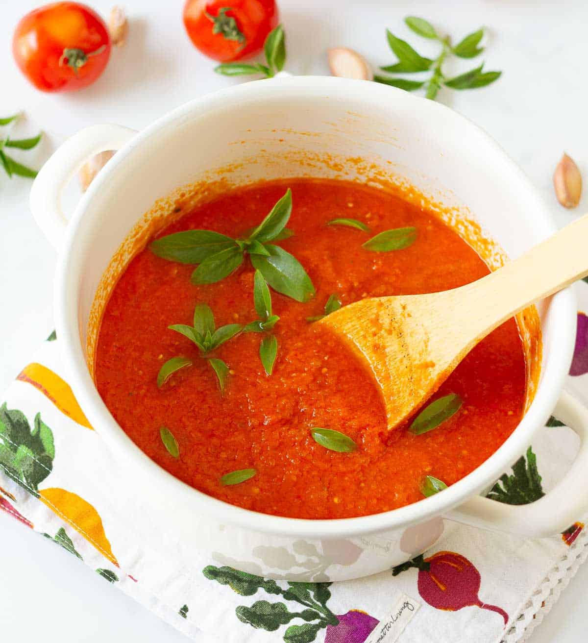 A white pot with tomato sauce and basil leaves and a wooden spoon in it.