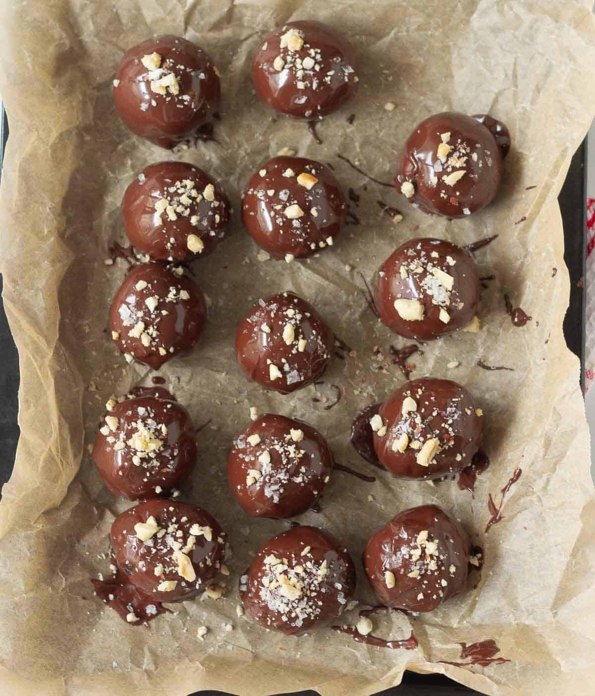 Energy balls dipped in chocolate and topped with peanuts and sea salt on parchment paper.
