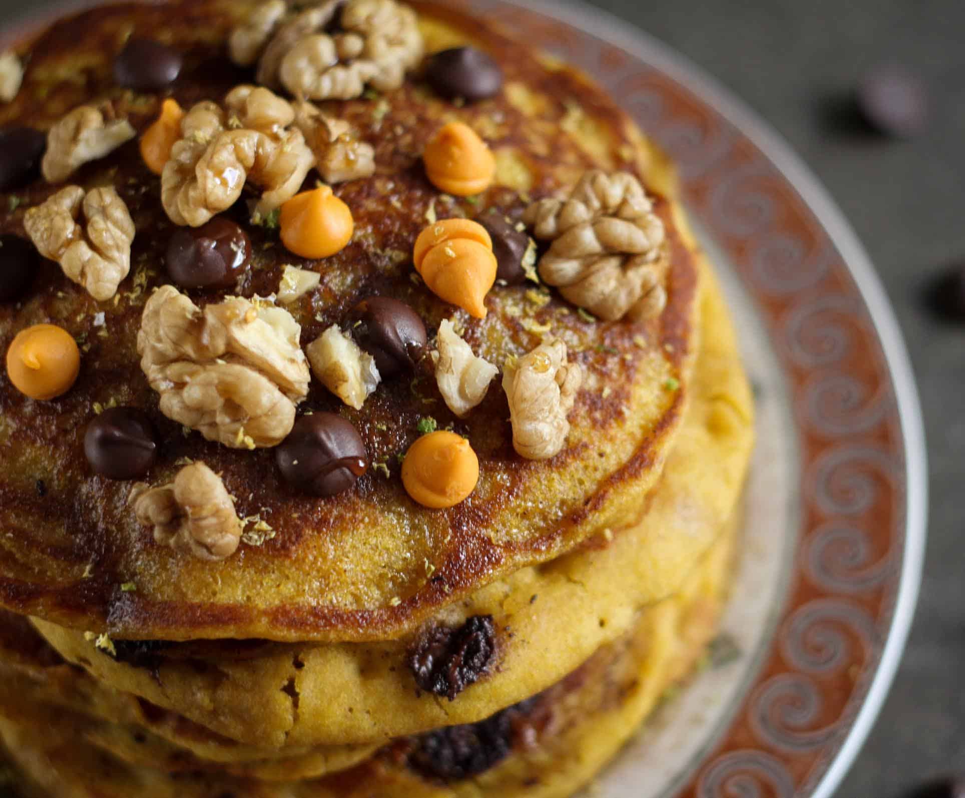 a stack of pumpkin orange pancakes topped with walnuts and chocolate chips.