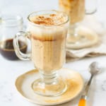 oatmeal latte in a clear glass mug on a small plate with a spoon.