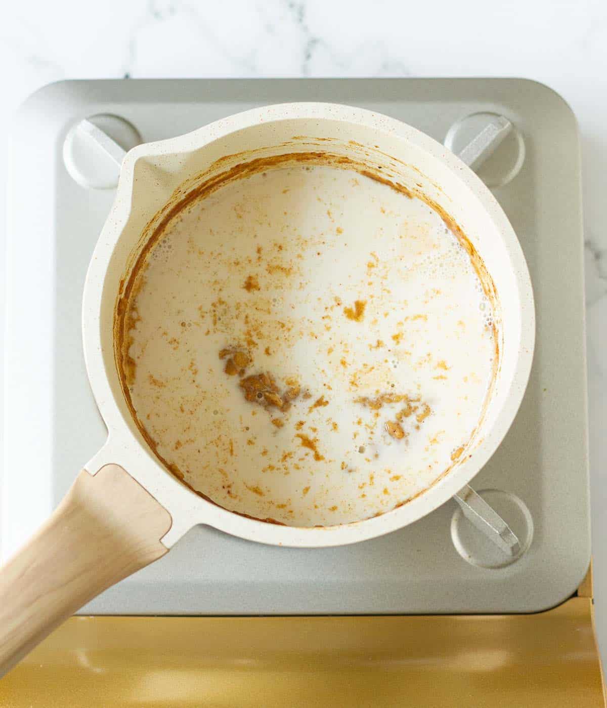 Coconut milk added to the oats mixture in a white saucepan on a stove.