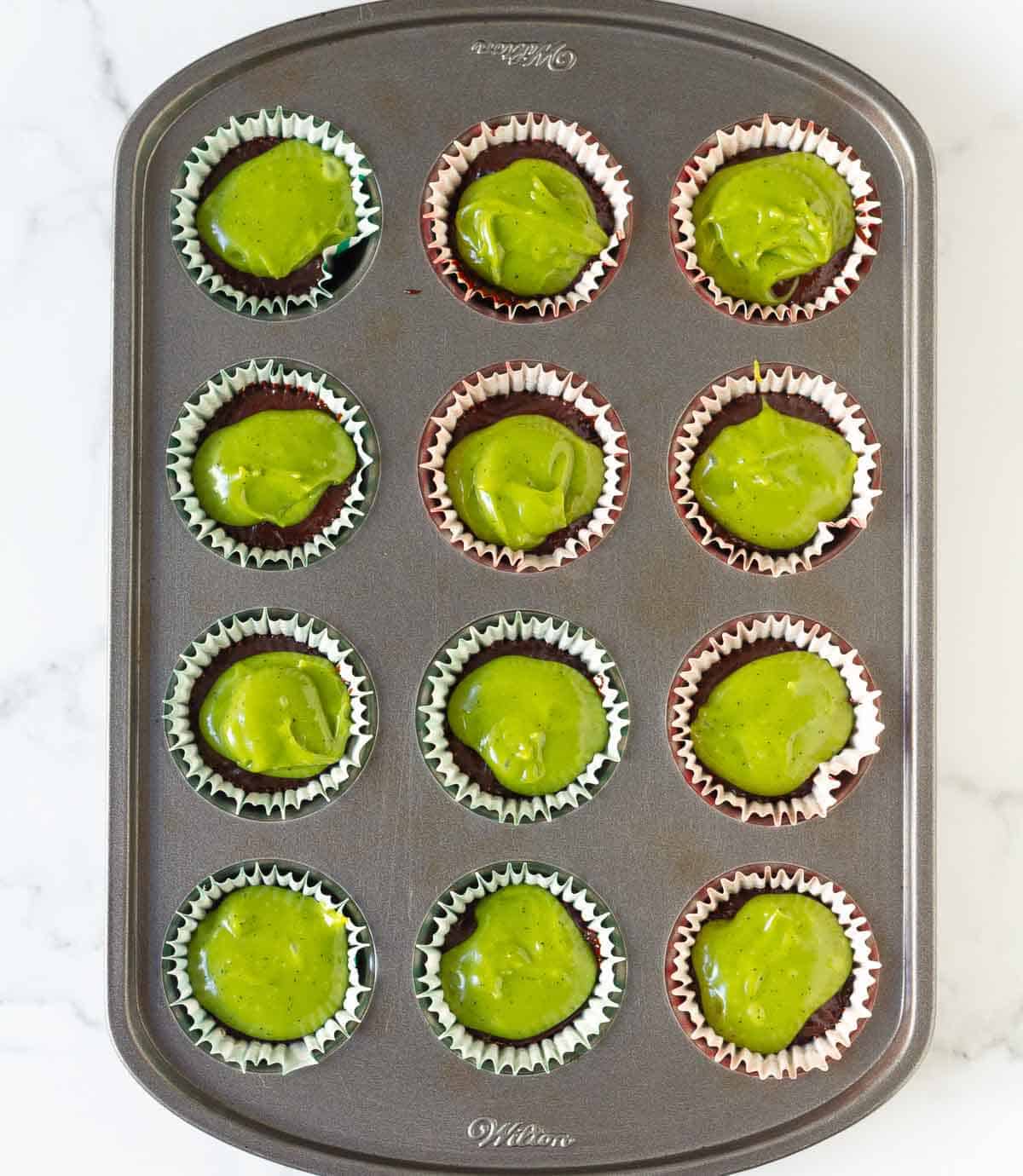 Matcha mixture on top of dark chocolate in mini muffin tray.