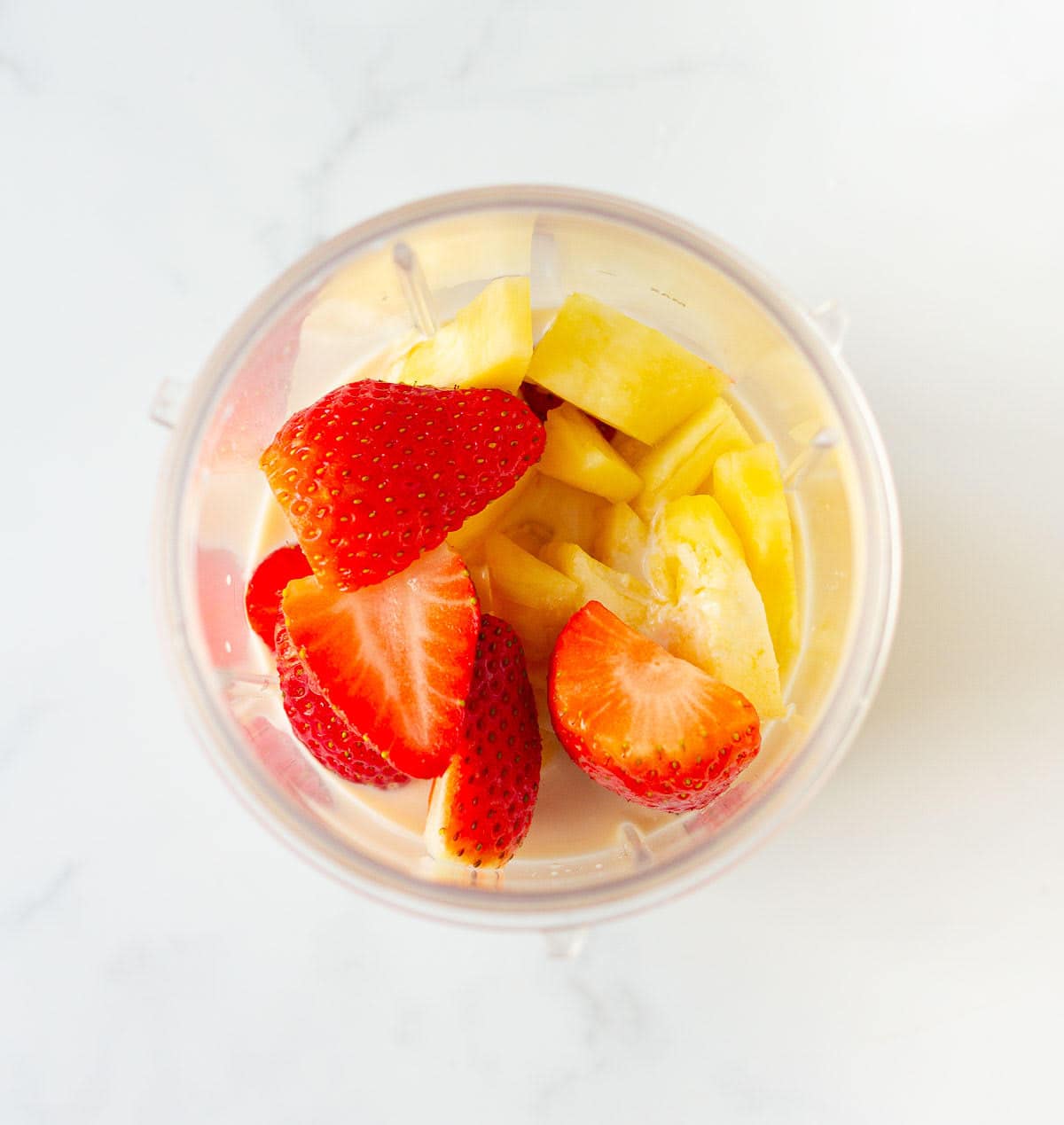 strawberries, banana, and pineapple with cashew milk in a blender jar.
