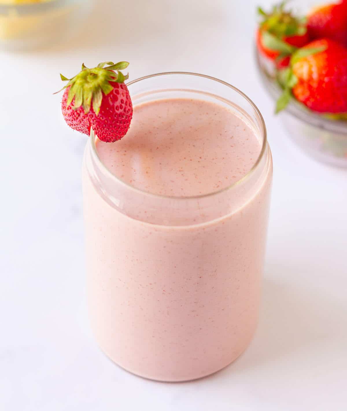 strawberry smoothie in a glass with a strawberry on the rim.